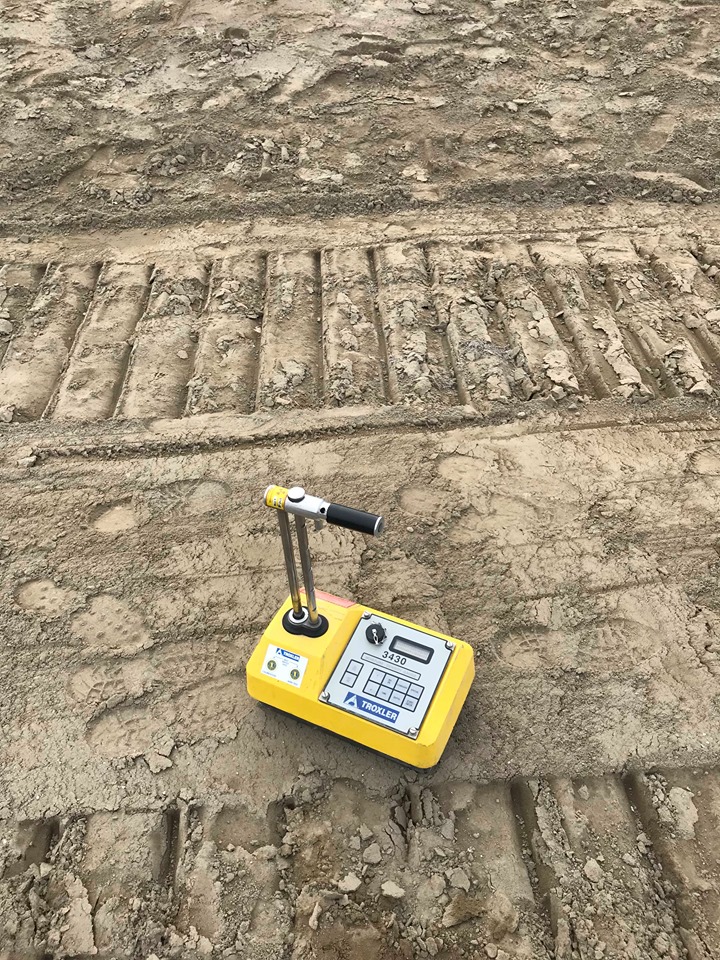 A yellow nuclear density gauge on a compacted soil surface