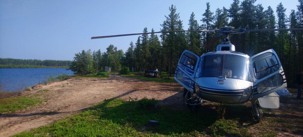 A-star helicopter with both front doors open at a landing site on the edge of a lake