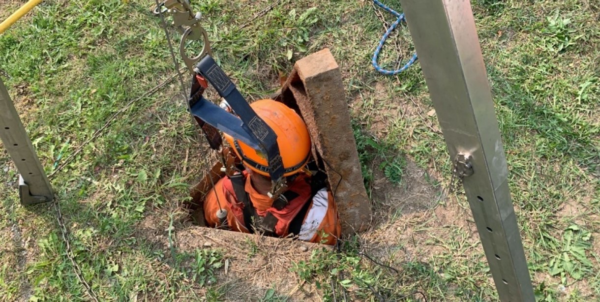 A man wearing orange PPE is being winched into a confined space.