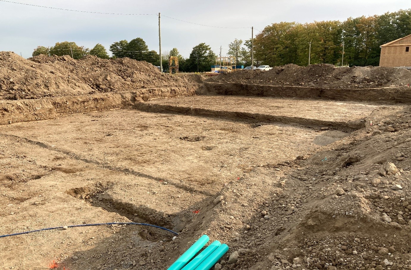 An area of excavated soil in a residential area. There are turquoise coloured pipes in the foreground. 